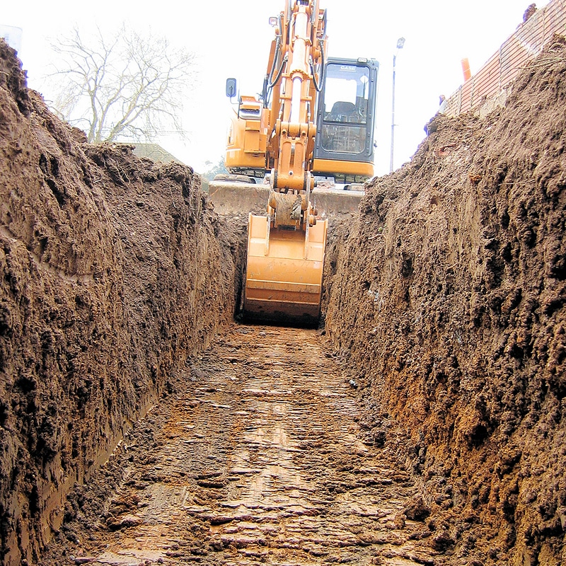 Pelle mécanique CASE creusant une tranchée étroite et profonde dans la terre boueuse, avec les parois abruptes du sol visible.